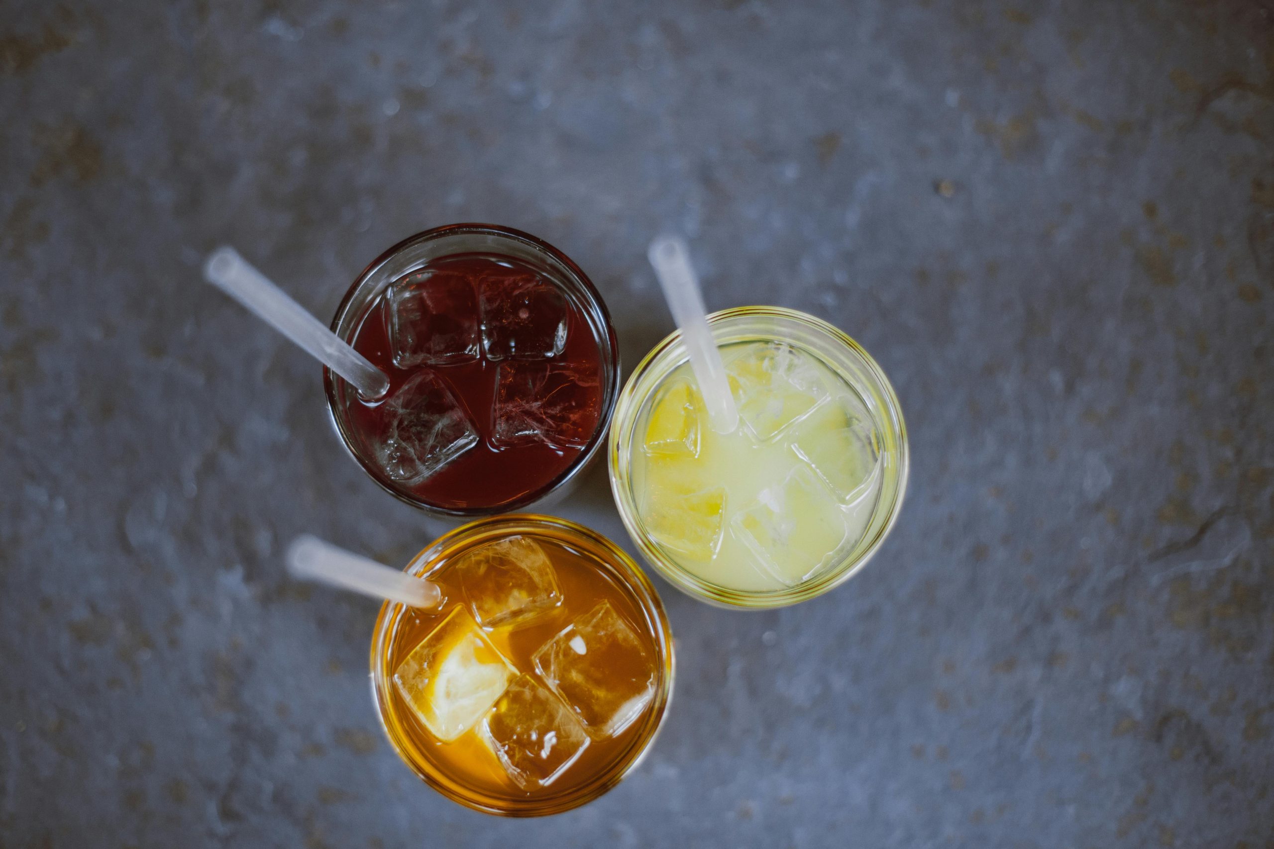 Top view of three refreshing iced juices with straws on a gray background.